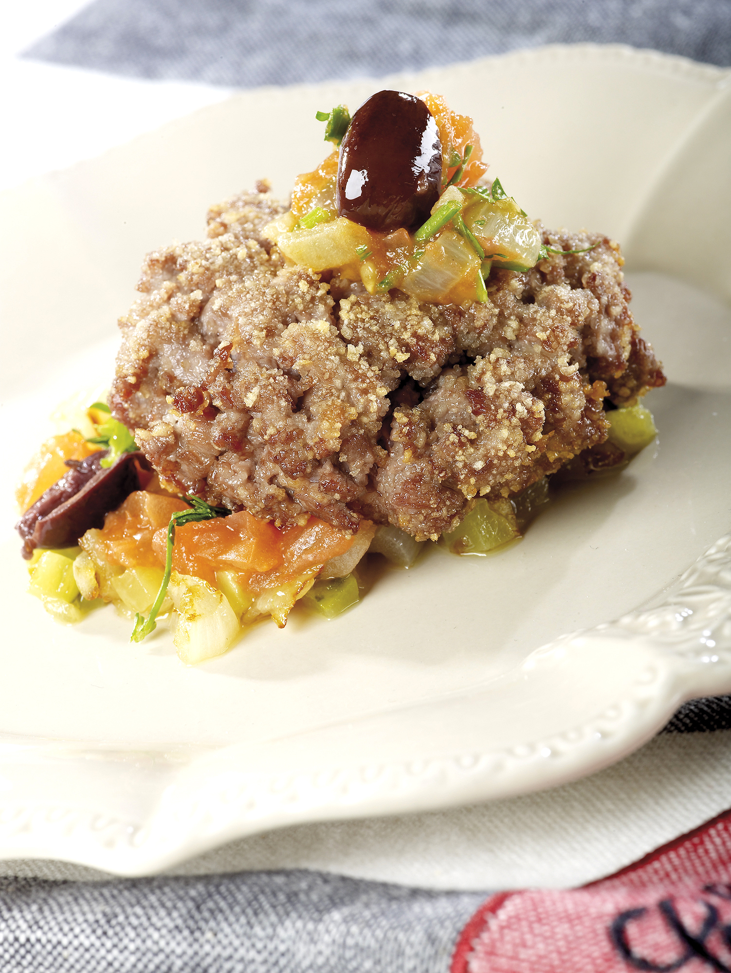 Kurz angebratenes Rinderhacksteak mit Cornichons, Petersilie, Zwiebeln, Tomaten und Oliven